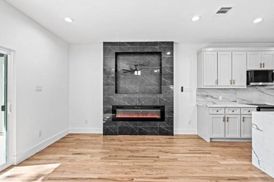 Kitchen with white cabinets, ceiling fan, light wood-type flooring, and a fireplace