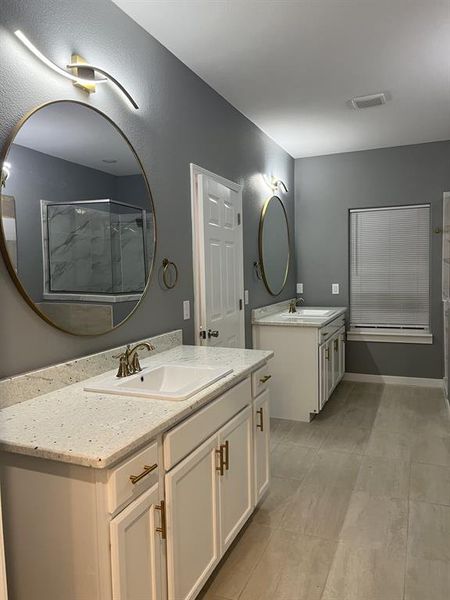 Full bath with two vanities, a shower stall, and light tile patterned floors Full bath with two vanities, a shower stall, and light tile patterned floors