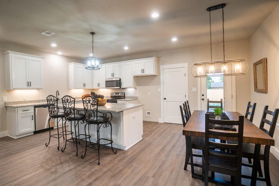 Kitchen with appliances with stainless steel finishes, a center island, white cabinets, wood finished floors, and light stone countertops Kitchen with appliances with stainless steel finishes, a center island, white cabinets, wood finished floors, and light stone countertops