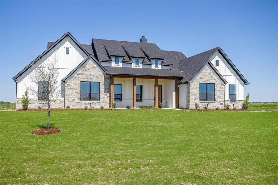 Modern farmhouse style home featuring board and batten siding, roof with shingles, a front yard, stone siding, and a chimney