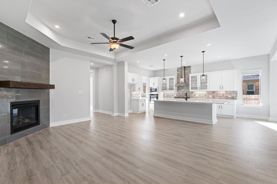 Unfurnished living room featuring a raised ceiling, a fireplace, light wood finished floors, a ceiling fan, and recessed lighting