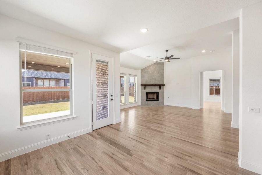 Open living room with hardwood floors, ceiling fan, and tile fireplace with wood mantel