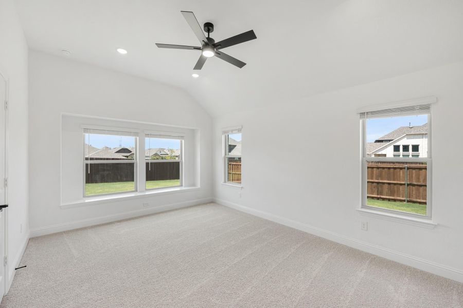 Empty bedroom with vaulted ceiling, ceiling fan, carpet flooring, and multiple windows overlooking backyard Empty bedroom with vaulted ceiling, ceiling fan, carpet flooring, and multiple windows overlooking backyard