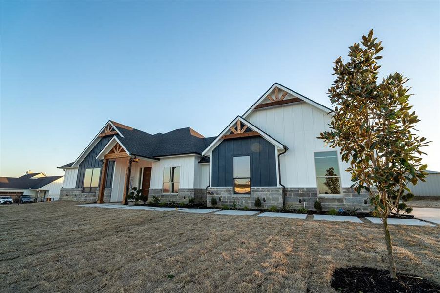 Modern farmhouse style home with stone siding, a front lawn, board and batten siding, and roof with shingles