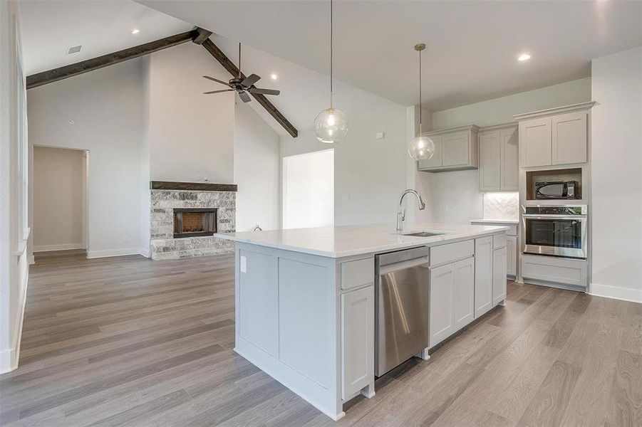 Kitchen featuring light hardwood / wood-style flooring, a stone fireplace, appliances with stainless steel finishes, sink, and beamed ceiling