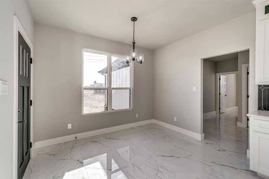 Unfurnished dining area featuring an inviting chandelier, baseboards, and marble finish floor