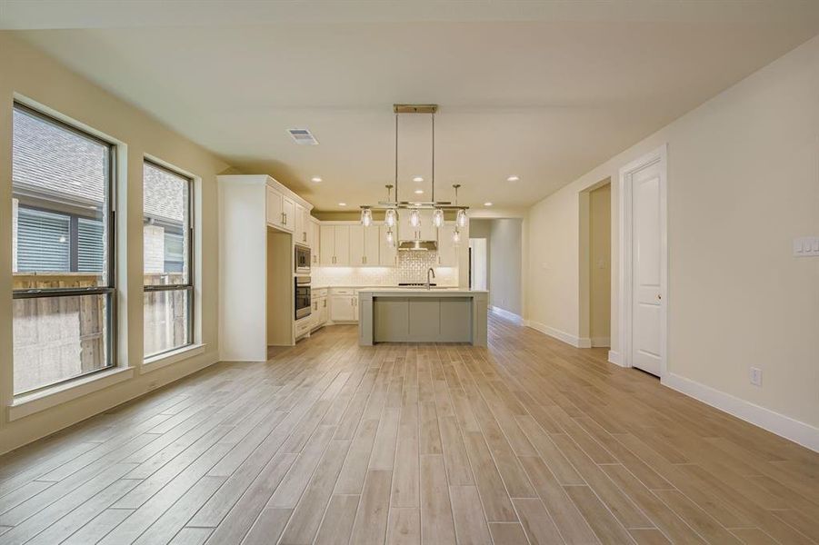 Kitchen with light countertops, decorative light fixtures, white cabinetry, an island with sink, and open floor plan