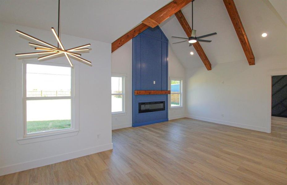 Unfurnished living room with a large fireplace, a chandelier, beam ceiling, light wood-style flooring, and high vaulted ceiling Unfurnished living room with a large fireplace, a chandelier, beam ceiling, light wood-style flooring, and high vaulted ceiling