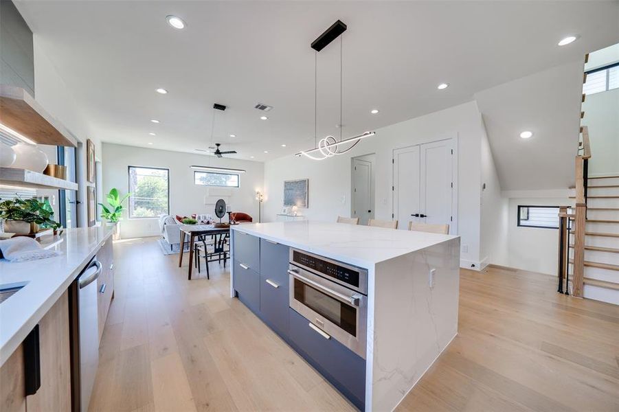 Kitchen featuring ceiling fan, light hardwood / wood-style flooring, stainless steel appliances, decorative light fixtures, and a center island