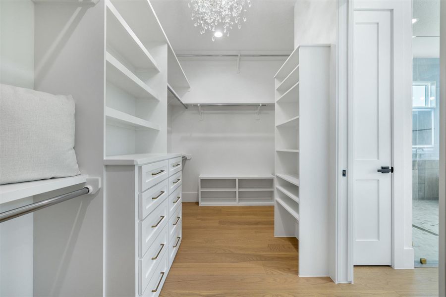 Spacious closet featuring light wood finished floors and a chandelier