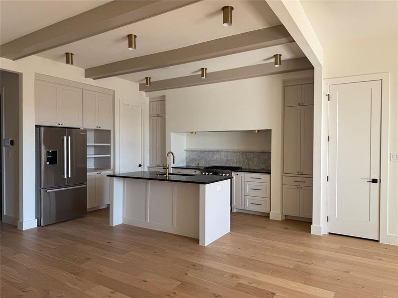 Kitchen with beam ceiling, decorative backsplash, sink, a kitchen island with sink, and stainless steel fridge