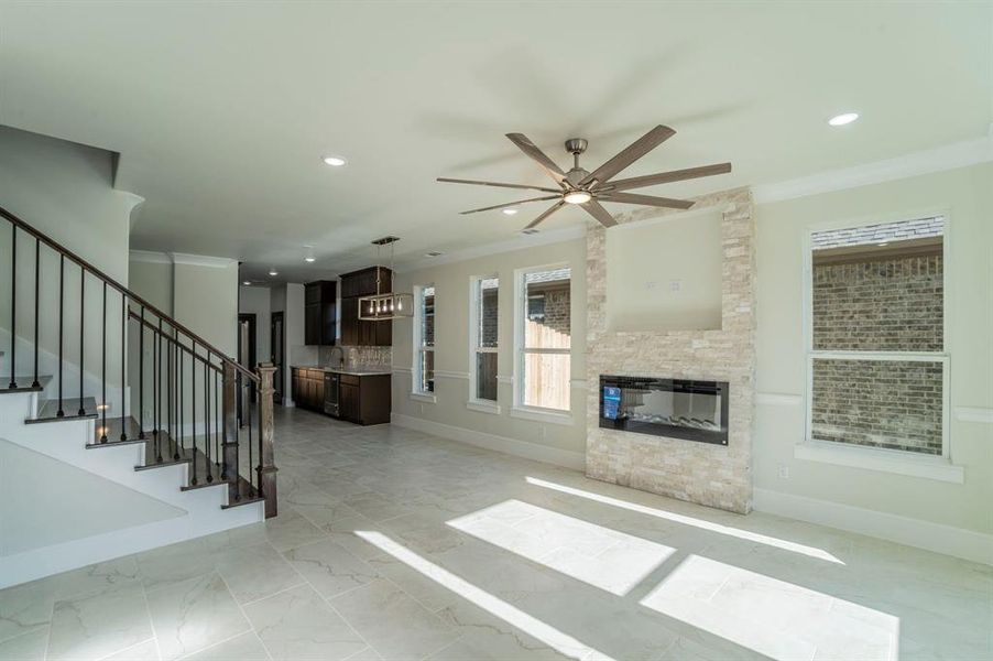 Unfurnished living room with stairs, crown molding, a ceiling fan, an outdoor stone fireplace, and recessed lighting Unfurnished living room with stairs, crown molding, a ceiling fan, an outdoor stone fireplace, and recessed lighting