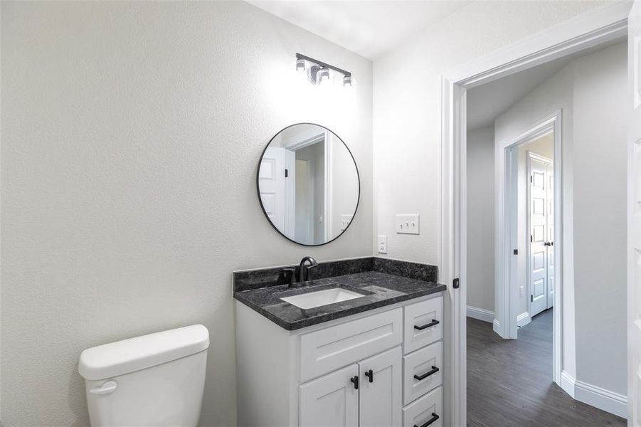 Bathroom featuring a white vanity with dark hardware, a dark speckled countertop, a rectangular undermount sink, a circular mirror, and dark wall-mounted lighting