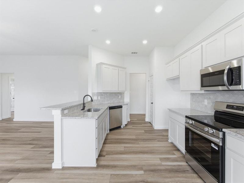 Kitchen featuring white shaker cabinetry, stainless steel appliances, light-colored countertops, and wood-finish flooring Kitchen featuring white shaker cabinetry, stainless steel appliances, light-colored countertops, and wood-finish flooring