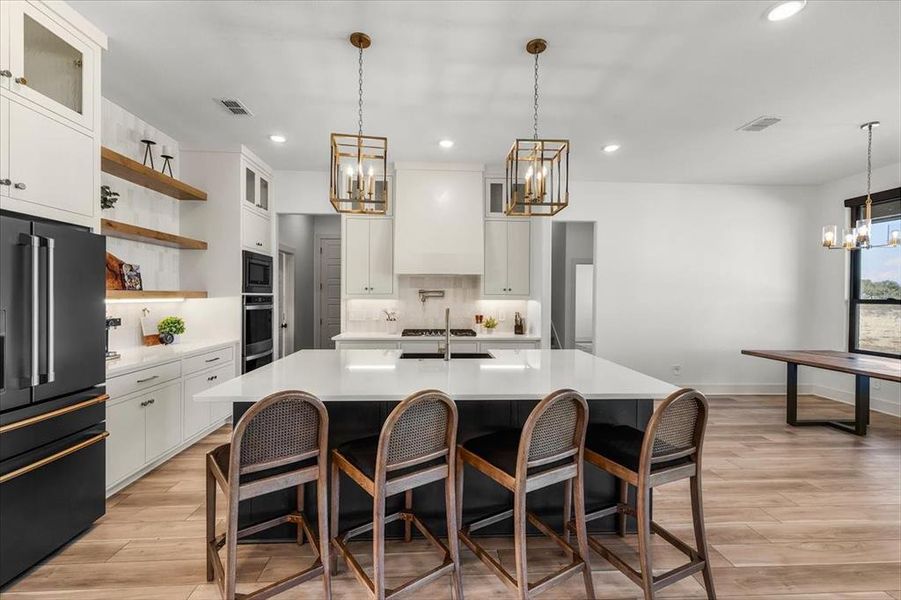 Stunning dual black-gold tone chandeliers over kitchen island with black farmhouse sink & quartz countertops.