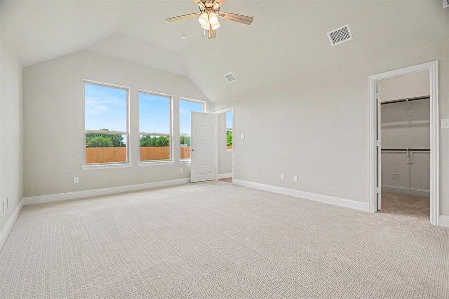 Spacious room featuring a vaulted ceiling with a ceiling fan, three large windows, textured carpet, and an open doorway revealing a closet with shelving and hanging rods Spacious room featuring a vaulted ceiling with a ceiling fan, three large windows, textured carpet, and an open doorway revealing a closet with shelving and hanging rods