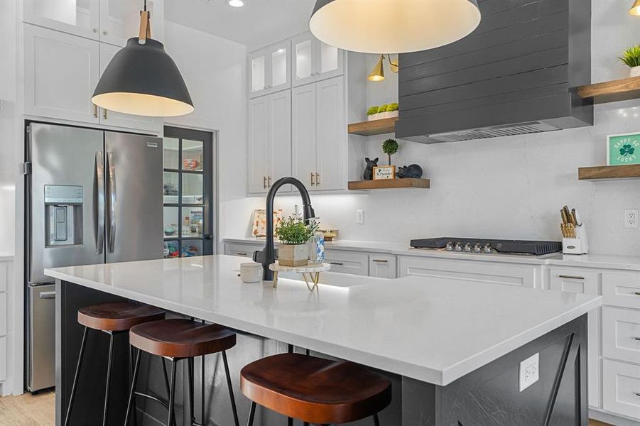 Kitchen with stainless steel appliances, a center island with sink, white cabinetry, wall chimney range hood, and open shelves Kitchen with stainless steel appliances, a center island with sink, white cabinetry, wall chimney range hood, and open shelves