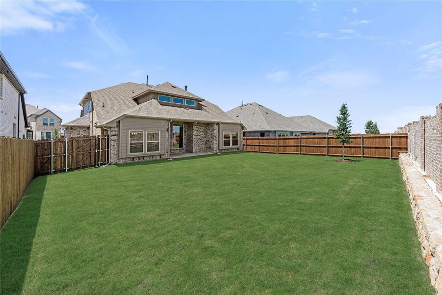 Spacious backyard with green lawn, wood privacy fence, and brick home with covered patio