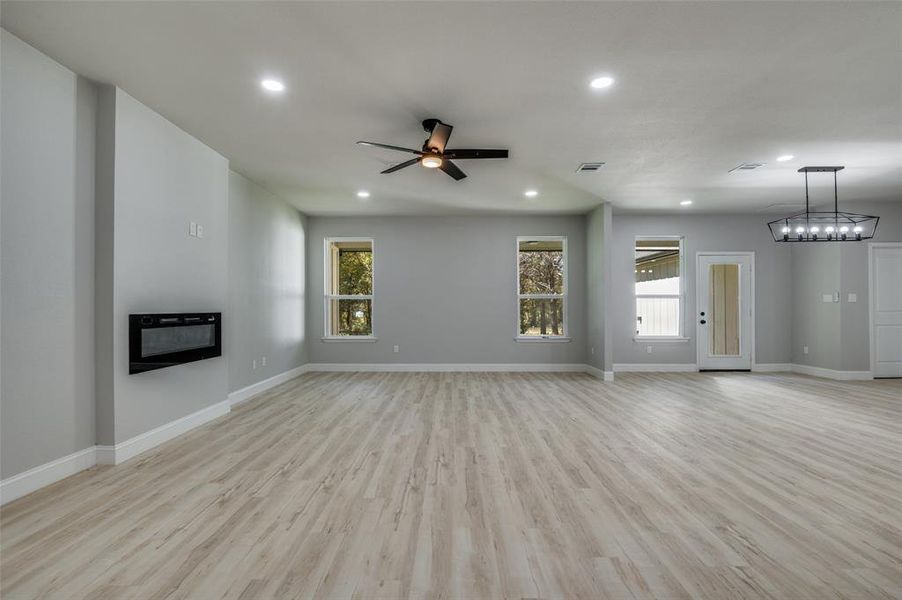 Unfurnished living room featuring light wood-style flooring, a glass covered fireplace, recessed lighting, a ceiling fan, and heating unit Unfurnished living room featuring light wood-style flooring, a glass covered fireplace, recessed lighting, a ceiling fan, and heating unit