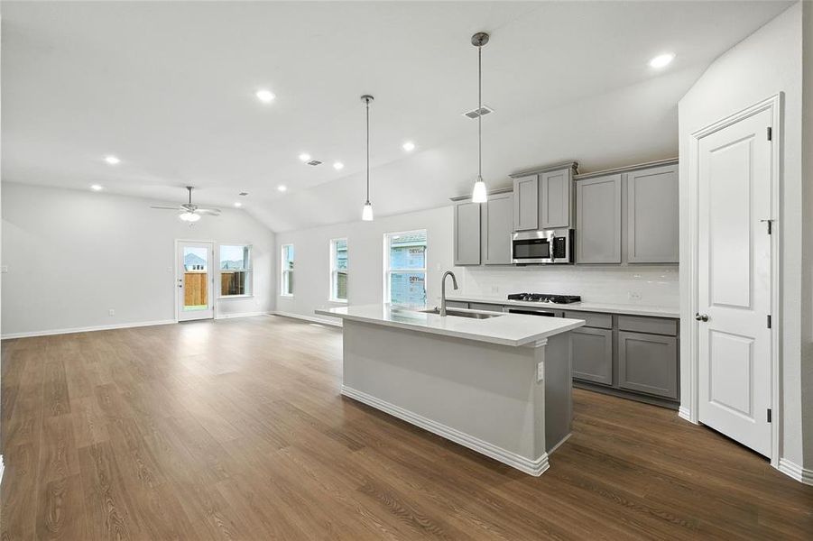 Kitchen featuring gray cabinets, vaulted ceiling, pendant lighting, backsplash, and an island with sink Kitchen featuring gray cabinets, vaulted ceiling, pendant lighting, backsplash, and an island with sink