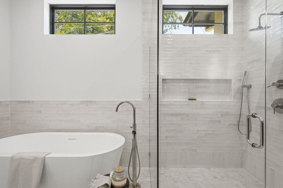 High windows illuminate a modern bathroom featuring a freestanding tub and walk-in glass shower.