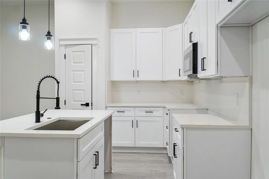 Kitchen featuring white cabinetry, pendant lighting, light wood-style floors, and an island with sink