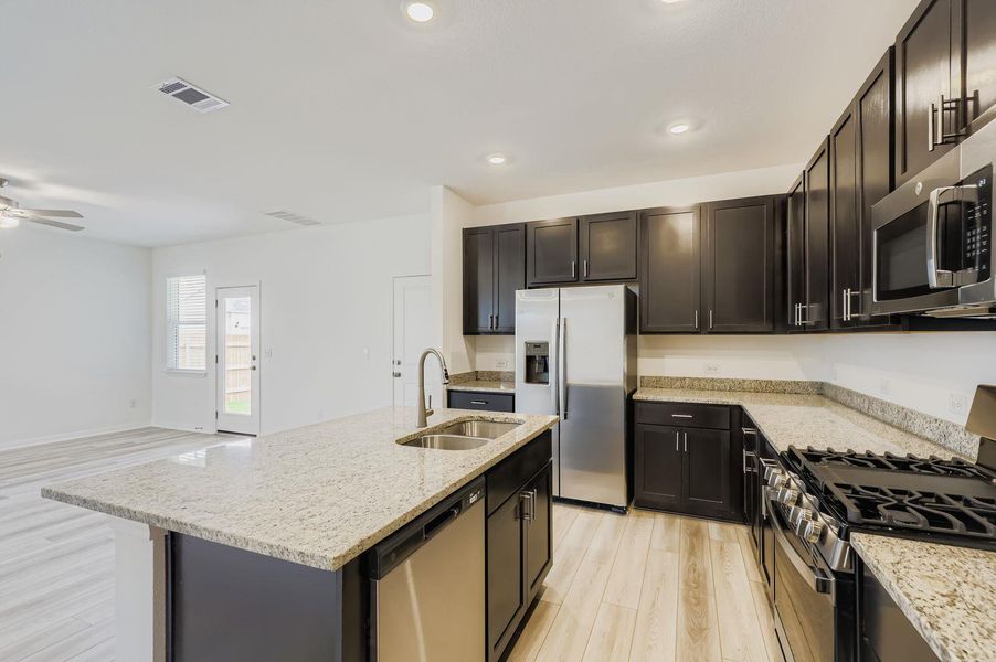 Kitchen with appliances with stainless steel finishes, light wood-type flooring, light stone countertops, open floor plan, and a kitchen island with sink Kitchen with appliances with stainless steel finishes, light wood-type flooring, light stone countertops, open floor plan, and a kitchen island with sink