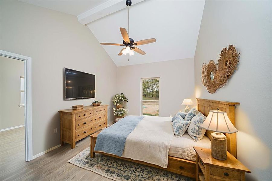 Bedroom featuring beamed ceiling, wood finished floors, high vaulted ceiling, and a ceiling fan Bedroom featuring beamed ceiling, wood finished floors, high vaulted ceiling, and a ceiling fan