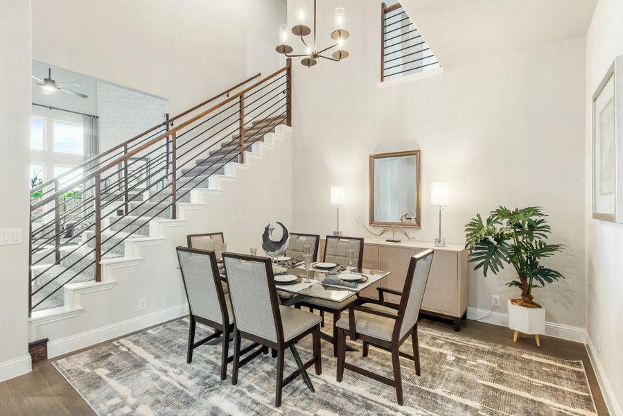Dining room with six-chair glass table, high ceilings, modern chandelier, and staircase with metal railing Dining room with six-chair glass table, high ceilings, modern chandelier, and staircase with metal railing