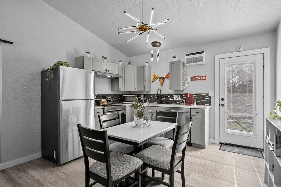 Kitchen with gray cabinets, stainless steel appliances, light wood finished floors, light countertops, and backsplash.
