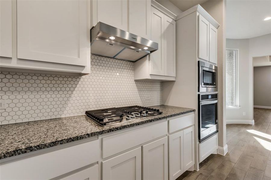 Kitchen featuring gas stove, stainless steel appliances, white cabinetry, ventilation hood, and light stone counters