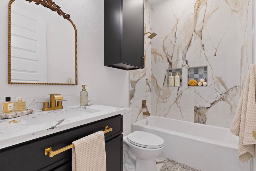 Luxurious bathroom with veined marble-look tile, a crisp white tub, and a modern dark wood vanity with gold hardware.