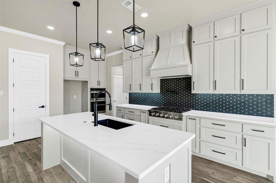 Kitchen featuring sink, custom exhaust hood, stainless steel gas stovetop, and a center island with sink