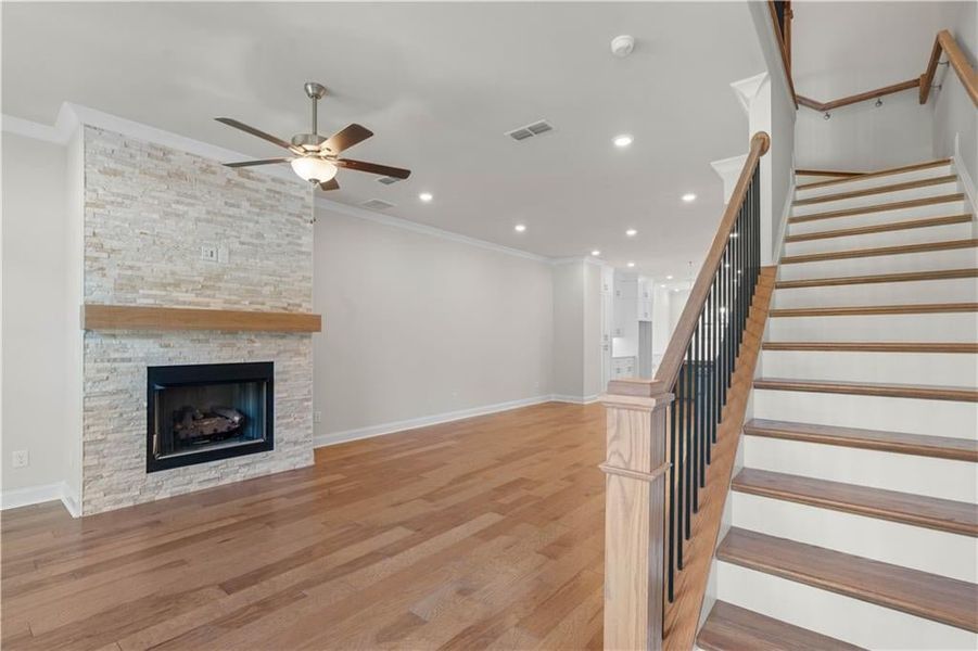 Unfurnished living room with ornamental molding, light wood-style flooring, recessed lighting, a fireplace, and stairway