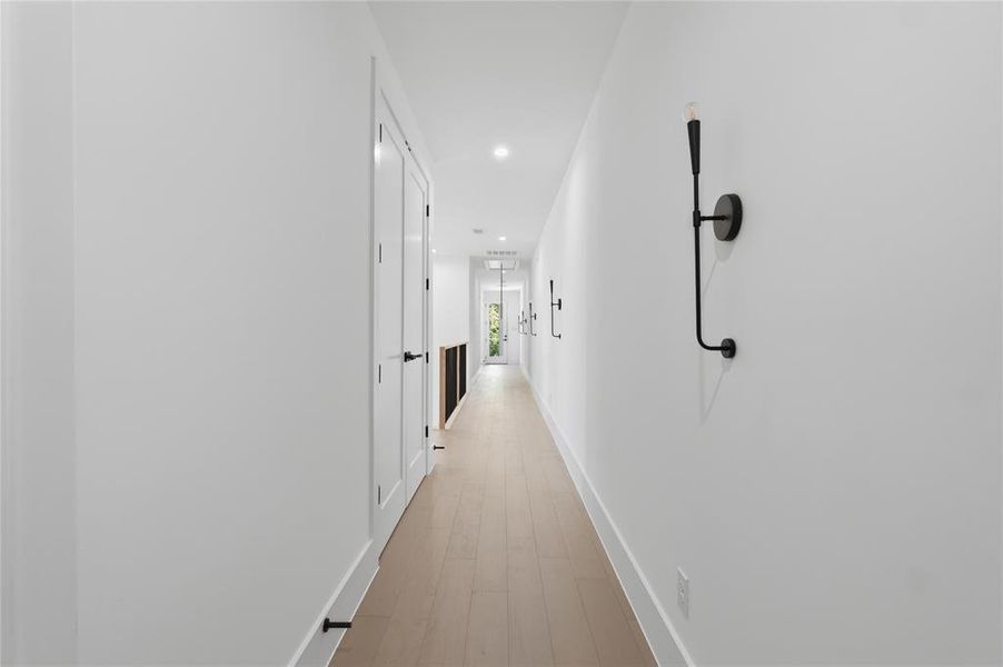 Hallway featuring light wood-finish flooring, white walls, and contemporary black wall sconces