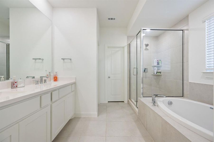 Bathroom featuring a stall shower, double vanity, a bath, and light tile patterned flooring