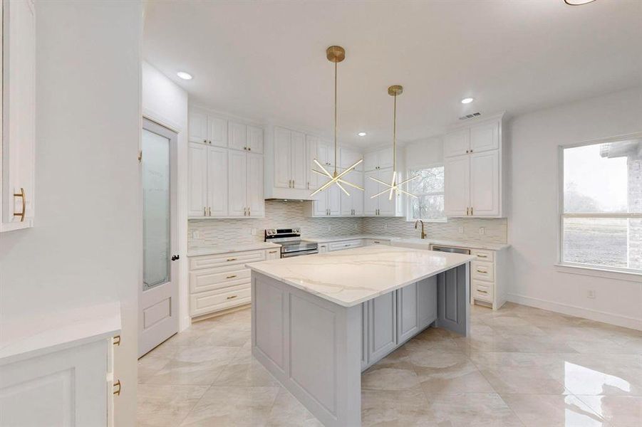 Kitchen with a chandelier, pendant lighting, stainless steel electric range oven, light stone counters, and a kitchen island