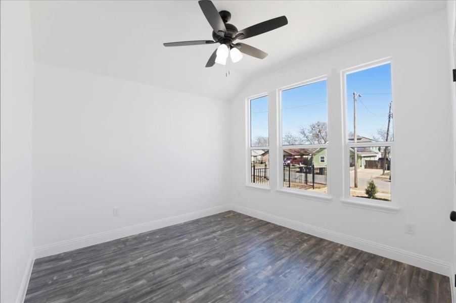 Empty room featuring dark wood-style floors, vaulted ceiling, a ceiling fan, and baseboards