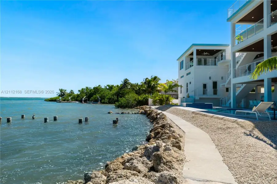 Multi-level coastal residence featuring deep-water access, a private swimming pool, concrete bulkhead, and tiered covered balconies Multi-level coastal residence featuring deep-water access, a private swimming pool, concrete bulkhead, and tiered covered balconies