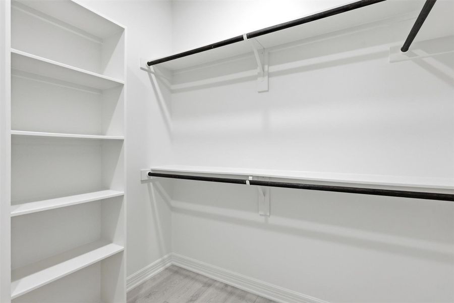 Spacious walk in closet with custom built in shelving and hanging rods on both sides.