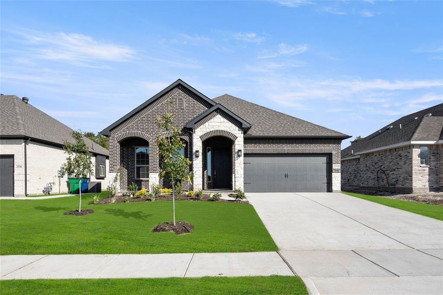 French country home featuring brick siding, an attached garage, concrete driveway, and a front lawn