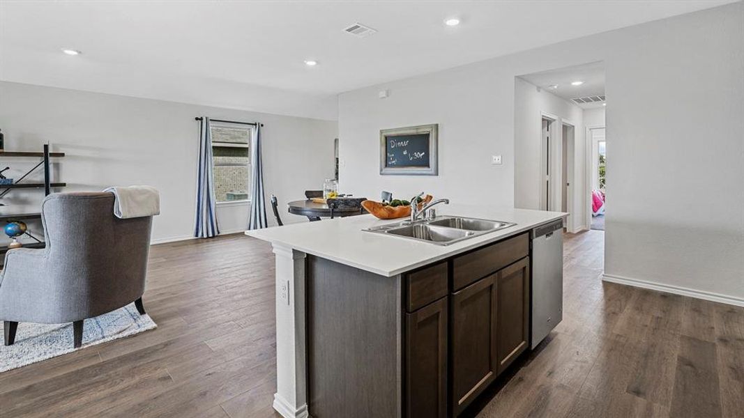 Kitchen island with integrated stainless steel sink and dishwasher, white countertops, recessed lighting, and wood-finish flooring throughout