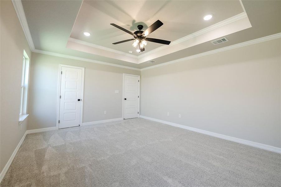 Unfurnished bedroom with a raised ceiling, ornamental molding, light colored carpet, ceiling fan, and recessed lighting
