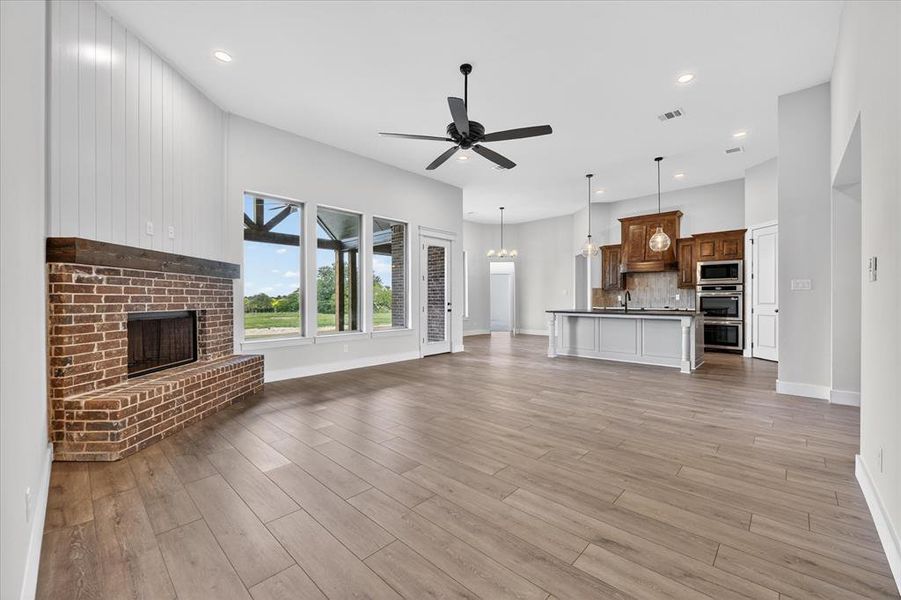 Unfurnished living room featuring a fireplace, a ceiling fan, light wood-style floors, and suspended lighting