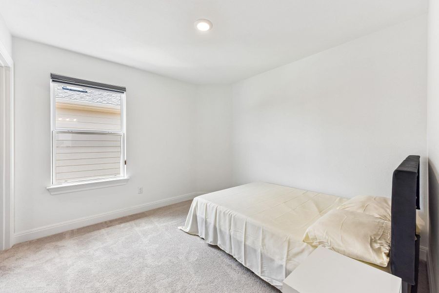 A well-lit bedroom features plush carpeting and a wide window offering natural illumination.