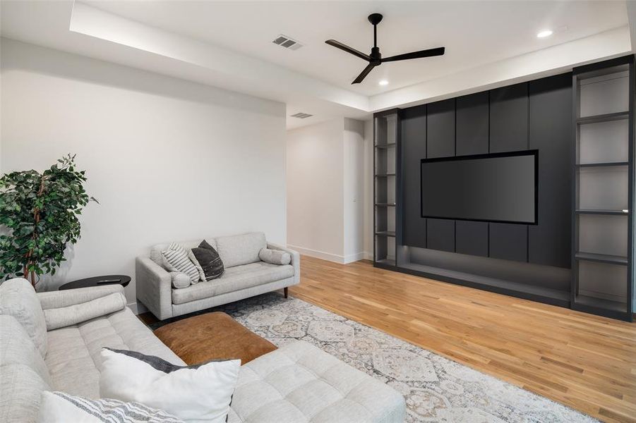 Spacious game room featuring hardwood floors, a tray ceiling, and a striking accent wall with custom built-ins designed for both style and function. The integrated media wall creates the perfect space for movie nights, gaming, or relaxing while the built-in shelving provides a stylish place to display décor and collectibles.