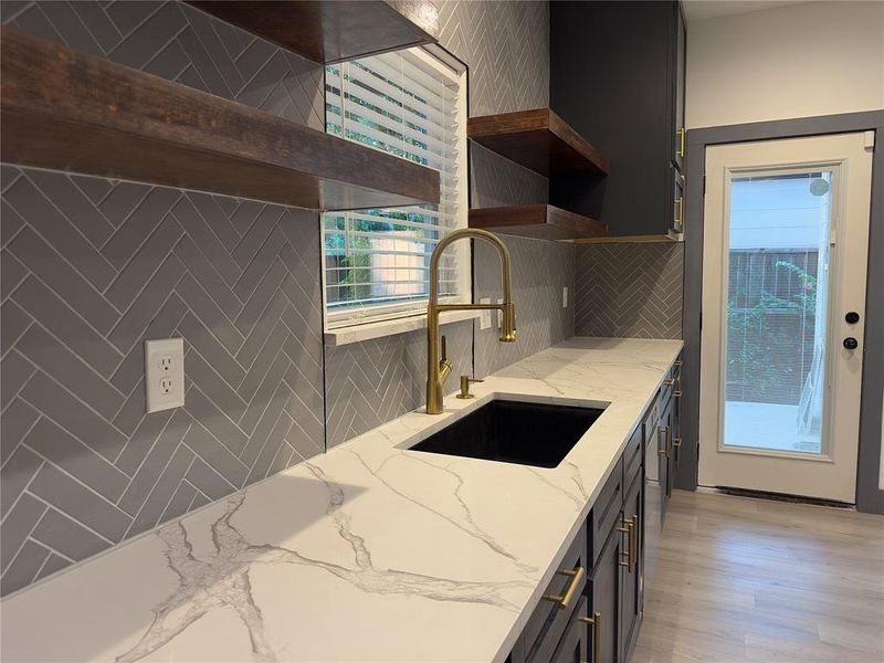 Kitchen with light hardwood / wood-style flooring, tasteful backsplash, dishwasher, light stone counters, and sink