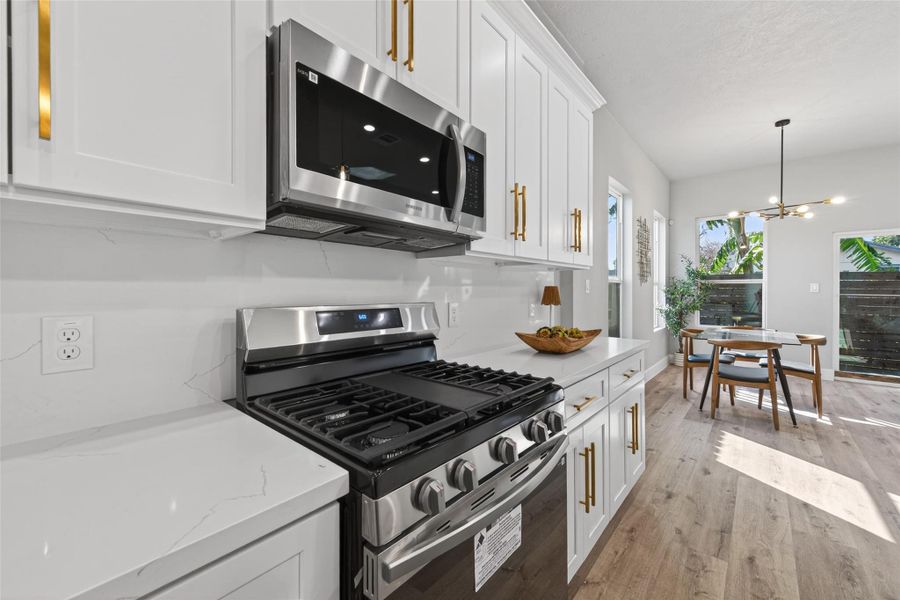Close-up view of premium finishes including quartz countertops, custom cabinetry, and a stainless steel gas range with five burners, paired with a built-in microwave for modern functionality.