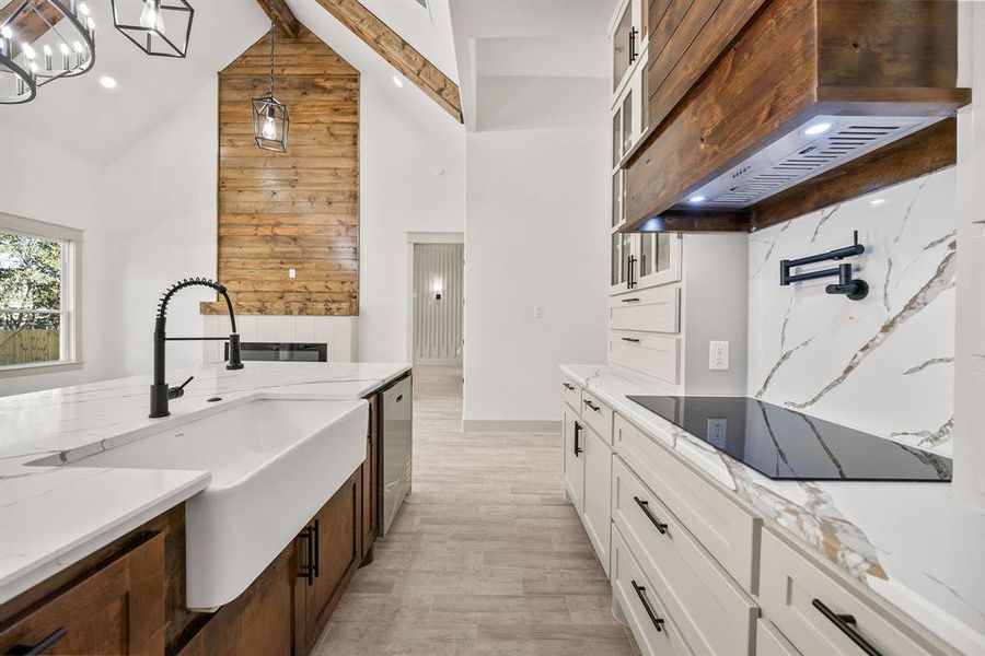 Kitchen featuring white cabinetry, glass insert cabinets, light stone counters, premium range hood, and high vaulted ceiling