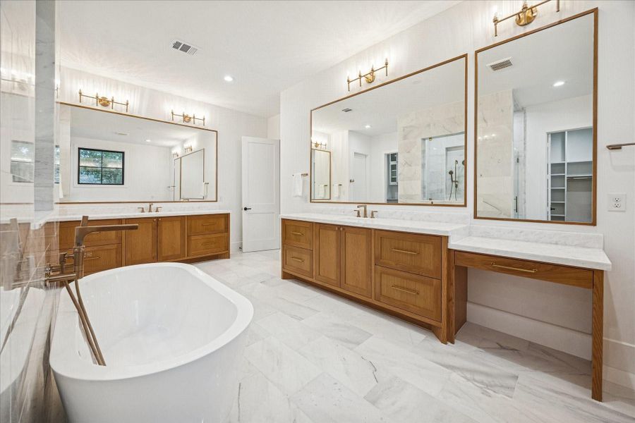 A long marble-topped vanity anchors the suite’s dressing area, complete with makeup counter, brass lighting, and a built-in beverage fridge. Sunlit windows provide a calming treetop backdrop. *Previous Project*